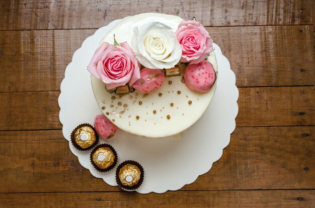 Schöner Kuchen verziert mit natürlichen Rosen und Pralinen auf Holztisch