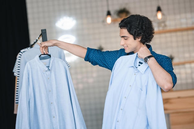 Schöner lächelnder junger Mann, der modische Hemden in der Boutique auswählt