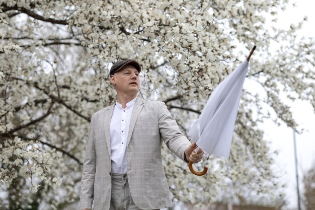 Schöner lächelnder Mann mit Regenschirm inmitten einer weißen blühenden Magnolie