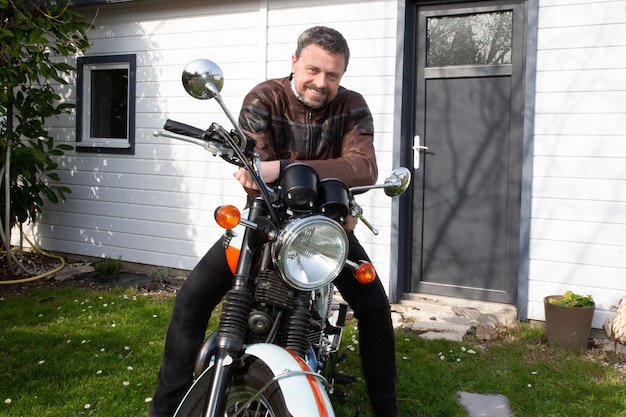 Schöner lächelnder mann mittleren alters in leder-motorradjacke fährt vintage-motorrad-neo-retro