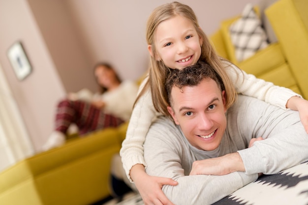 Schöner lächelnder Vater und Tochter, die sich im Wohnzimmer amüsieren und in die Kamera schauen.