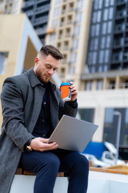 Schöner Lifestyle-Mann, der mit Laptop arbeitet Junger erfolgreicher Geschäftsmann macht eine Kaffeepause auf der Straße