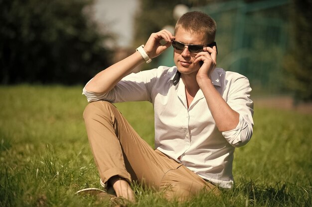 Schöner Macho genießt Sommertag Geschäftsmann mit Sonnenbrille im sonnigen Außenbereich Mann entspannt sich auf grünem Gras Modestil und Trend Break Time Konzept