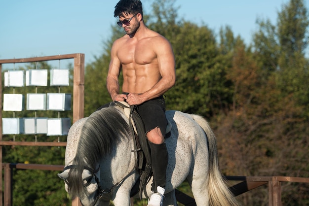 Schöner Macho-Mann-Cowboy, der auf einem Pferdehintergrund von Himmel und Bergen reitet