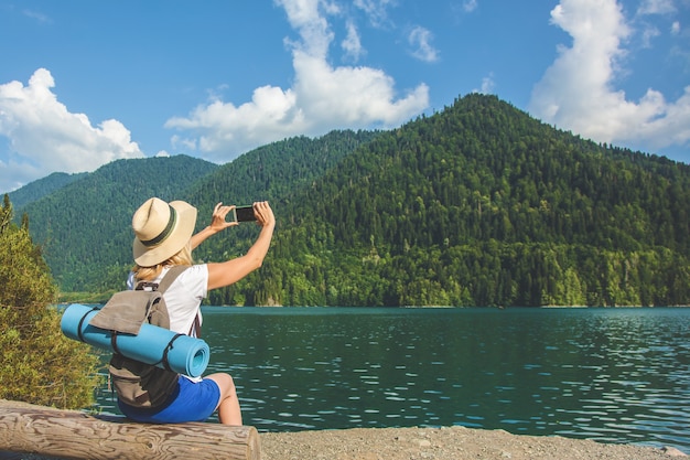 Schöner Mädchen-Reisender macht Fotos von einem großen blauen Gebirgssee im Hintergrund der Berge