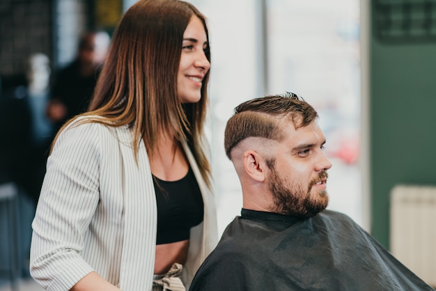 Schöner Mädchenfriseur schneidet einen bärtigen Mann im Salon