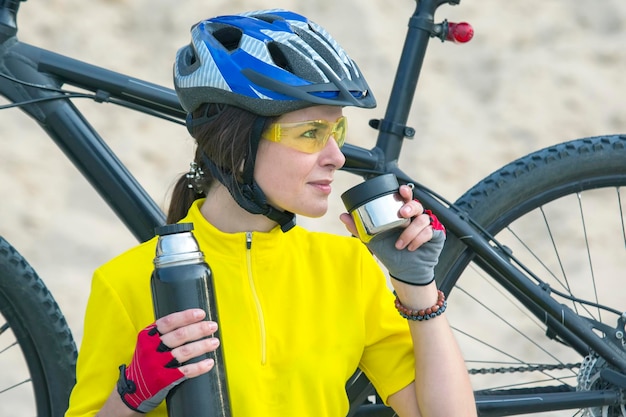 Schöner Mädchenradfahrer im Gelb mit Tee und Thermoskanne in der Hand