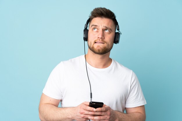 schöner Mann an der blauen Wand, die Musik mit einem Handy hört und denkt