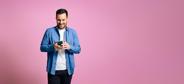 Schöner Mann, der ein Mobiltelefon auf rosa Hintergrund benutzt