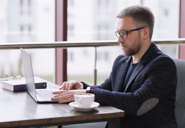 Schöner Mann, der in einem Restaurant am Laptop für eine Tasse Kaffee arbeitet