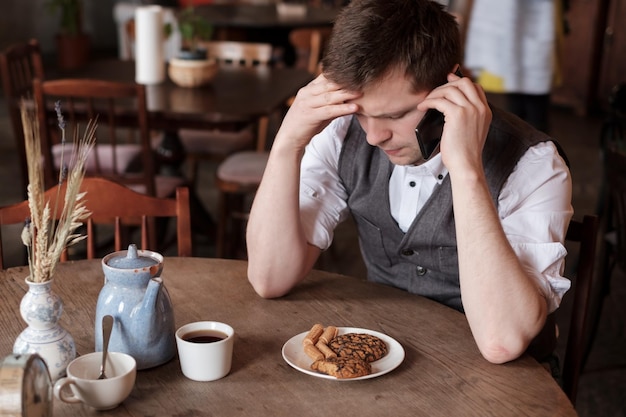 Schöner Mann, der Kaffee mit Keksen trinkt und ein ernstes Gespräch am Telefon führt