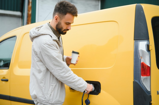 Schöner Mann, der Kaffee trinkt, während er Elektroauto auflädt