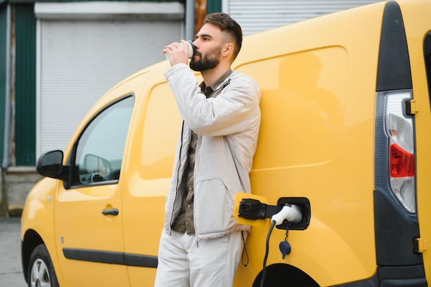 Schöner Mann, der Kaffee trinkt, während er Elektroauto auflädt