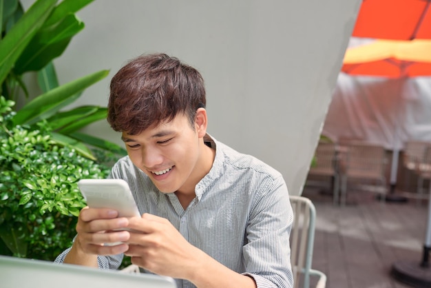 Schöner Mann, der mit Smartphone und Dokumenten im Café im Freien arbeitet