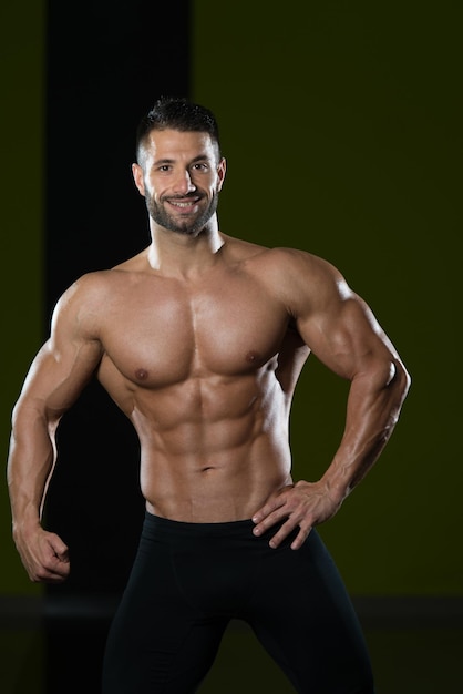 Schöner Mann, der stark in der Turnhalle steht und Muskeln beugt Muskulöser athletischer Bodybuilder Fitness Model posiert nach Übungen