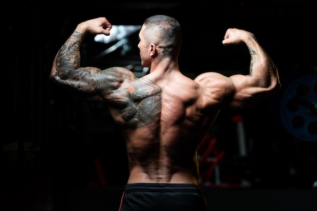 Schöner Mann, der stark in der Turnhalle steht und Muskeln beugt Muskulöser athletischer Bodybuilder Fitness Model posiert nach Übungen