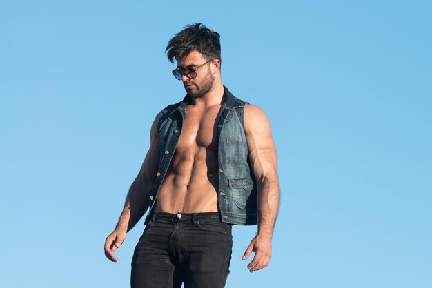 Schöner mann, der stark steht und im freien posiert und schwarze jeans trägt hintergrund des himmels