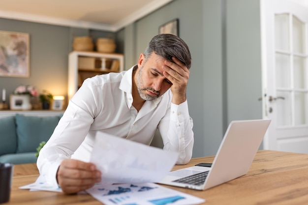 Schöner Mann Freelancer, der Informationen für die Planung von Projekten notiert, Remote-Arbeit über einen Laptop leistet, Mann, der E-Mails auf einem modernen Laptop liest