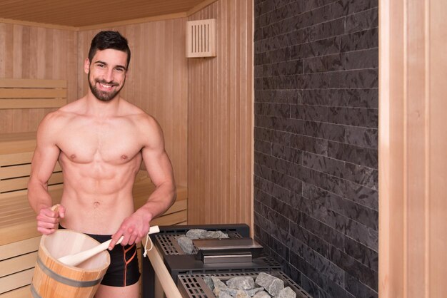 Schöner Mann gießt Wasser auf Hot Rocks in der Sauna