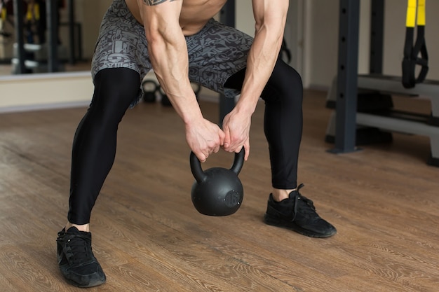 Schöner mann hockt mit kettlebell im fitnessstudio