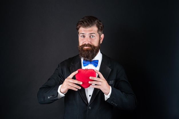 Schöner Mann im Smoking mit Liebesgeschenk des Herzens zum Valentinstag Valentinstag