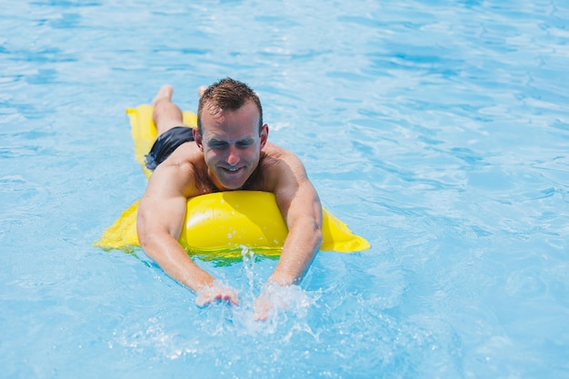 Schöner Mann in Badehose mit aufblasbarer gelber Matratze im Pool Sommerurlaub im Hotel