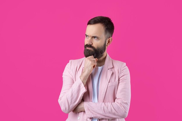 Schöner Mann mit Bart in rosa Jacke denkt über einen isolierten roten Hintergrund nach