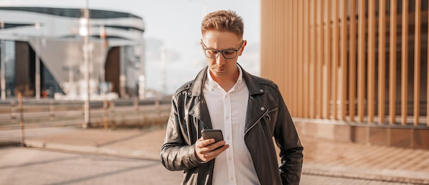 Schöner Mann mit Brille mit Smartphone auf der Straße einer Großstadt Geschäftsmann telefoniert im städtischen Hintergrund