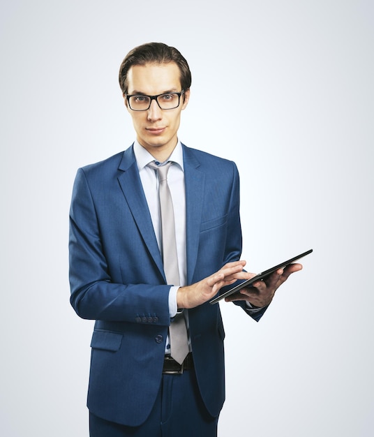 Schöner Mann mit Brille und klassischem Anzug mit digitalem Tablet isoliert auf hellgrauem Hintergrund