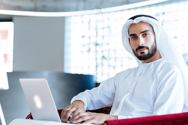 Schöner Mann mit Dish Dasha, der in seinem Geschäftsbüro in Dubai arbeitet