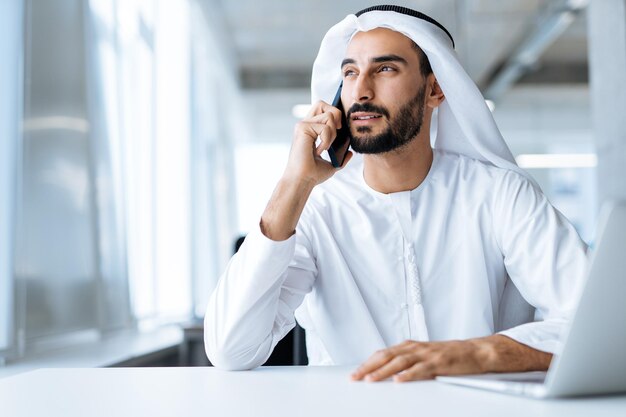 Schöner Mann mit Dish Dasha, der in seinem Geschäftsbüro in Dubai arbeitet