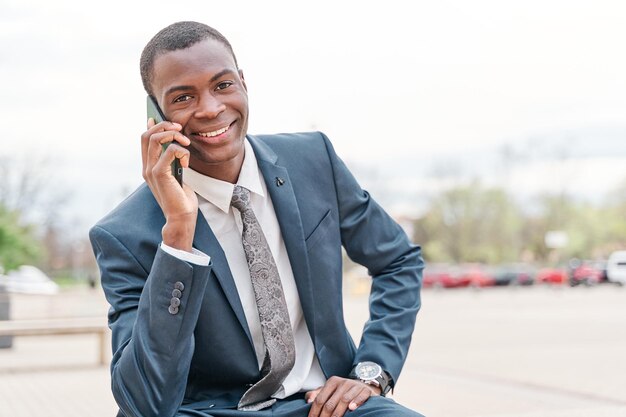 Schöner Mann mit einem Gespräch über ein Handy Young African American Geschäftsmann in Anzug und Krawatte Blick in die Kamera