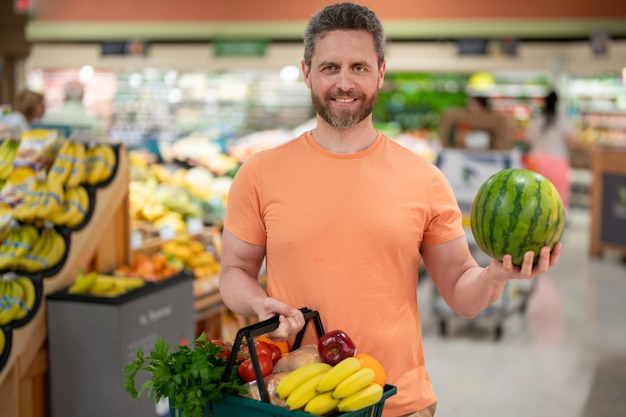 Schöner Mann mit Einkaufskorb mit Lebensmittelgeschäft Mann kauft Lebensmittel im Supermarkt männliches Modell in sho