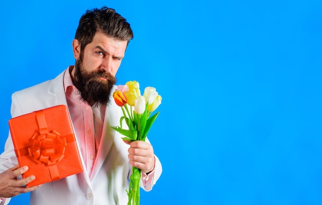 Schöner Mann mit Geschenk und Blumenstrauß aus Tulpen Geschenk zum Valentinstag Geburtstag der Frauen