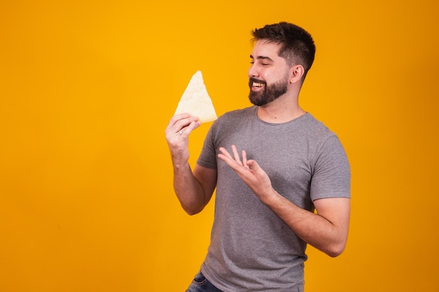 Schöner Mann mit Stück Käse auf gelbem Hintergrund. Junge mit einer Scheibe Käse in der Hand, die auf ihn zeigt