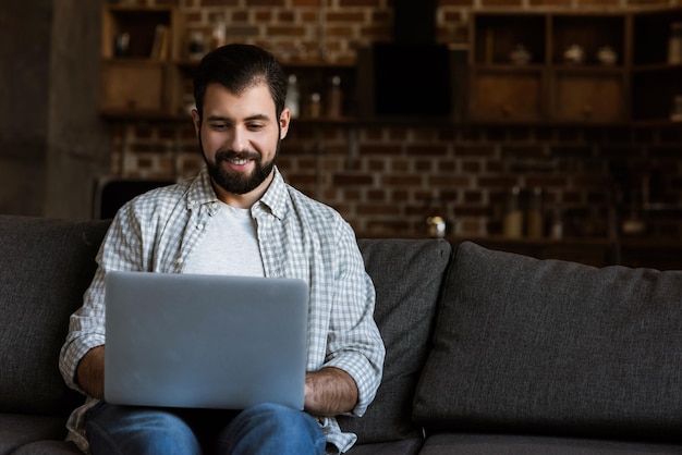 Schöner Mann sitzt auf der Couch und benutzt Laptop