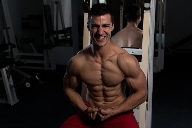 Schöner Mann sitzt stark im Fitnessstudio und lässt Muskeln spielen Muskulöser athletischer Bodybuilder Fitness Model posiert nach Übungen