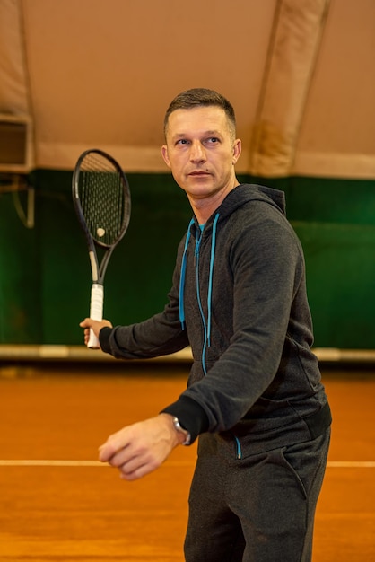 Schöner Mann steht vor Tennisspiel auf geschlossenem Tennisplatz mit Schläger in den Händen