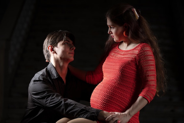 Schöner Mann umarmt eine schöne schwangere Frau auf dunklem Hintergrund