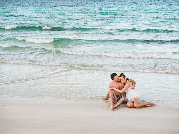 Schöner Mann und hübsche Frau sitzen am Strand mit Meereshintergrund und schauen in die Ferne. Im Freien, Nahaufnahme. Konzept von Freizeit und Reisen