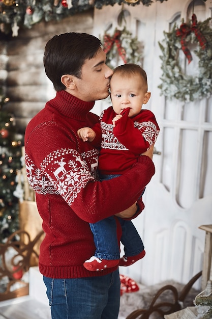 Schöner Mann und sein kleiner Sohn in hässlichen Pullovern im weihnachtlich dekorierten Interieur