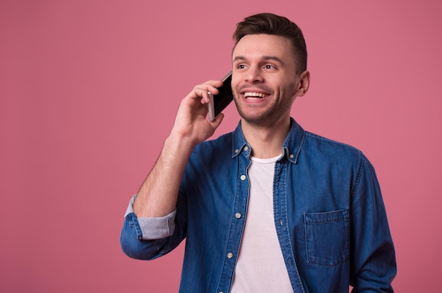 Schöner moderner Gelegenheitsmann spricht auf Smartphone isoliert auf rosa Hintergrund