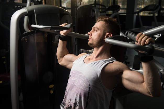 Schöner muskulöser Fitness-Bodybuilder, der im Fitnessstudio schwere Übungen für die Schultern an der Maschine macht