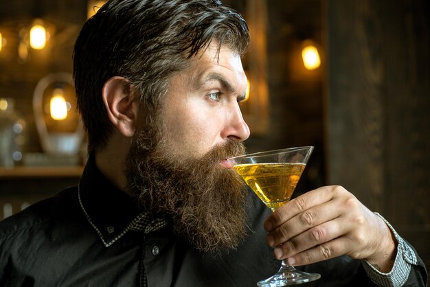 Schöner nachdenklicher Mann hält ein Glas Martini. Schöner Mann, der Alkohol trinkt, während er an der Bar sitzt.
