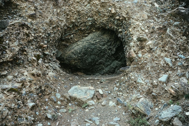 Schöner Naturhintergrund mit großem schwarzem Stein im Loch im Berg. Minimalistische Berglandschaft mit großem schwarzen Felsbrocken in dunkler Felshöhle, Nahaufnahme. Atmosphärischer Naturminimalismus in den Bergen.