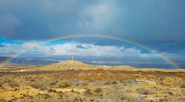 Schöner Regenbogen in trockener Lage mit Windmühlen und Bergen im Hintergrund.