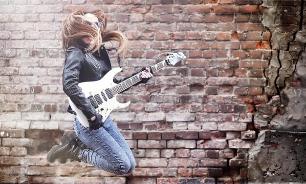 Schöner Rocker des jungen Mädchens mit E-Gitarre. Ein Rockmusikermädchen in einer Lederjacke mit Gitarre singt. Ein Solist einer Rockband spielt Gitarre und schreit ins Mikrofon.