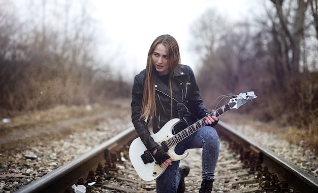 Schöner Rocker des jungen Mädchens mit E-Gitarre. Ein Rockmusikermädchen in einer Lederjacke mit Gitarre singt. Ein Solist einer Rockband spielt Gitarre und schreit ins Mikrofon.