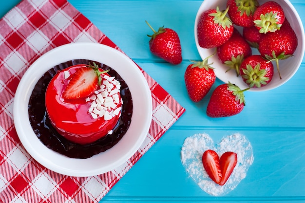 Schöner roter Erdbeerkuchen und eine Schüssel Erdbeeren auf einem blauen hölzernen Hintergrund