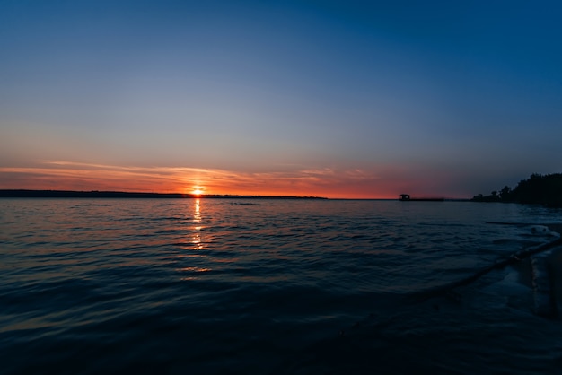 Schöner Sonnenuntergang am Fluss mit ausgehender roter Sonne und blauem Himmel